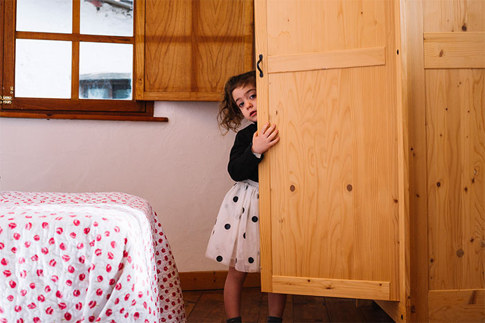 Young girl peeking from behind a wooden closet door, evoking creepy and unexplained experiences in a bedroom setting.