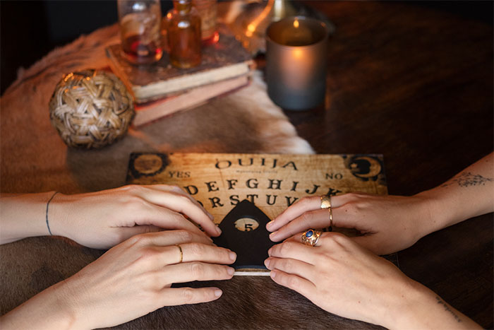 Two people using a Ouija board during a spooky session, experiencing creepy unexplained phenomena together.