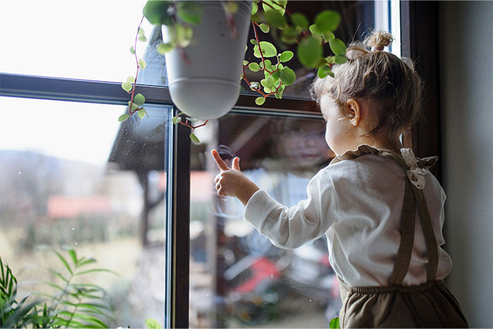 Young child touching window glass, reflecting outside view, evoking mysterious and creepy experiences people can’t explain.