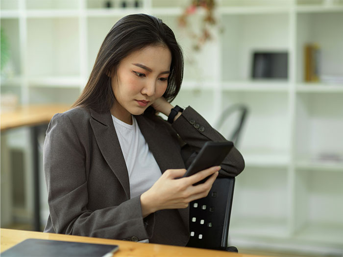 Young woman looking suspicious and confused while using her phone, experiencing creepy things she can't explain indoors.