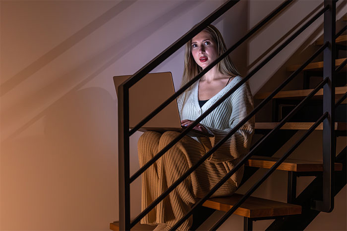 Woman sitting on stairs at night with laptop, looking startled, illustrating creepy things people have experienced.