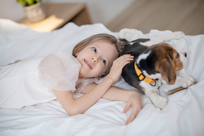 Young girl lying on bed with puppy, illustrating people can't explain these creepy things they’ve experienced moments.