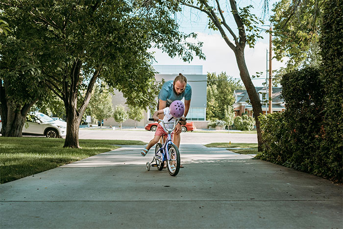 Man helping child learn to ride a bike on a sunny suburban street, capturing a moment from creepy things people experienced.
