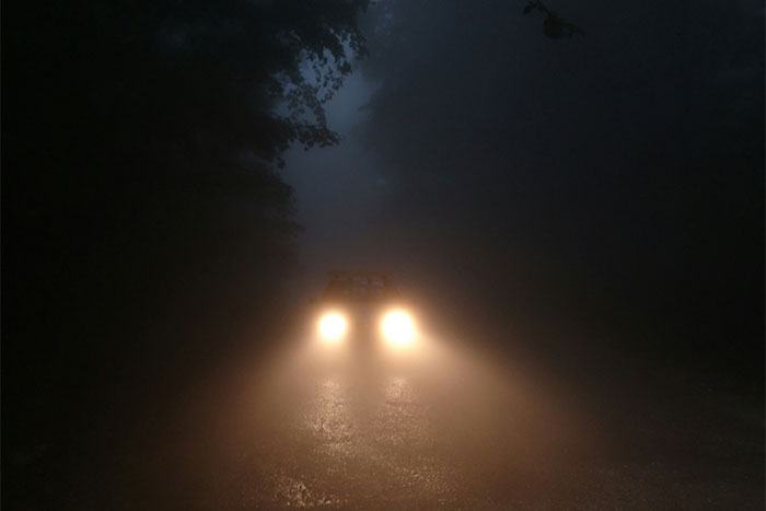 Car headlights shining through dense fog on a dark, creepy road, evoking unexplained eerie experiences.