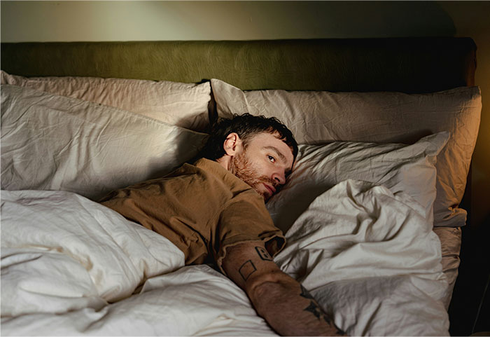 Man lying awake in bed looking unsettled, illustrating creepy experiences people can’t explain at night.