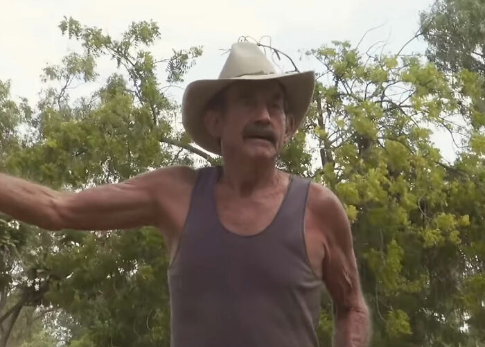 Elderly man in a sleeveless shirt and cowboy hat talking outdoors surrounded by trees in disappearance cases context