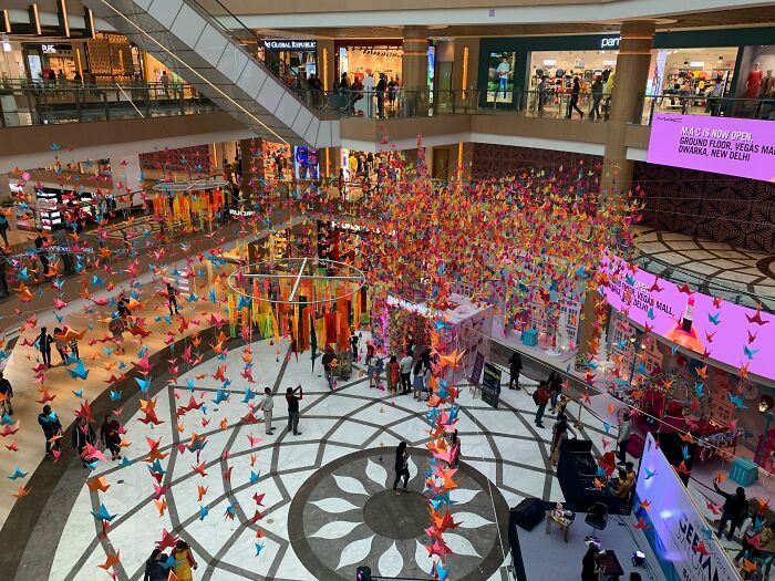 Colorful paper cranes art installation inside a shopping mall with crowds, related to disappearance cases theme.