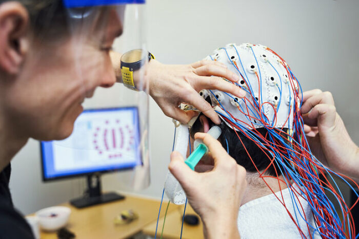 Scientist fitting a brain monitoring cap with electrodes on a person, exploring gut feeling and precognition research.