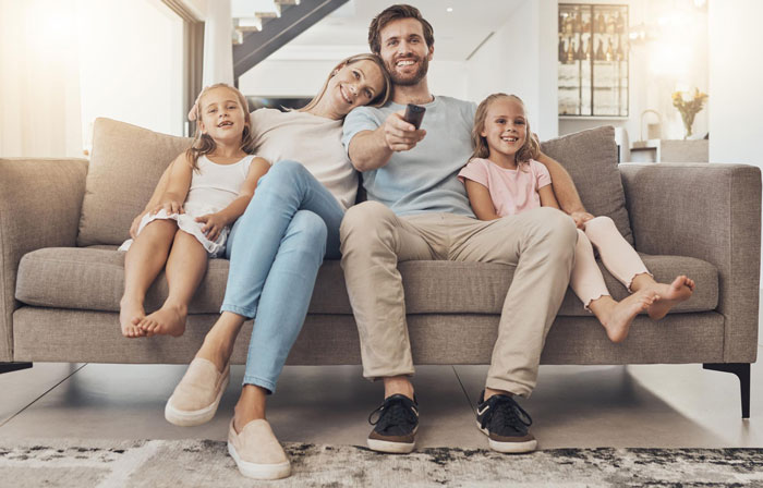 Family cuddling on couch with dad and daughters, showing a warm and affectionate family moment at home.