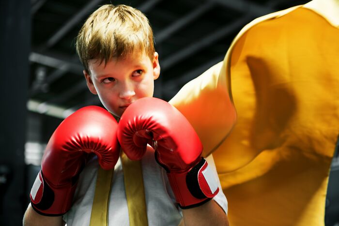 Young boy wearing red boxing gloves training in a school gym, highlighting shocking school incidents involving students and staff.