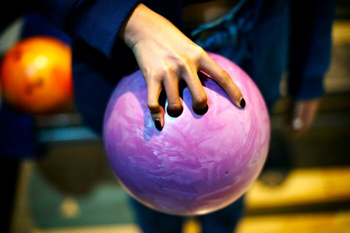 Hand holding a pink bowling ball at a bowling alley, illustrating fast ways someone can get fired.