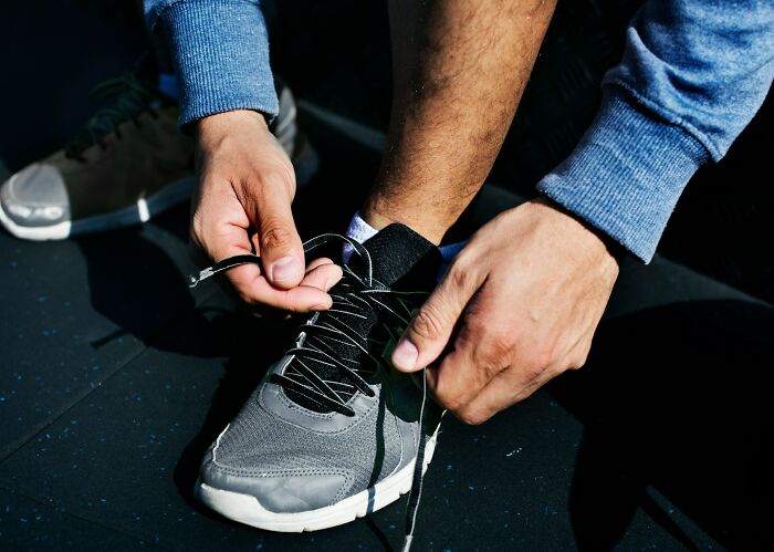 Adult hands tying shoelaces on gray sneaker, illustrating everyday things that humble fully grown adults in daily life.