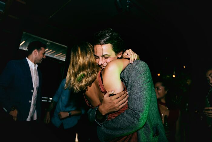 People sharing things they would never admit in real life, hugging closely at a dimly lit social gathering.