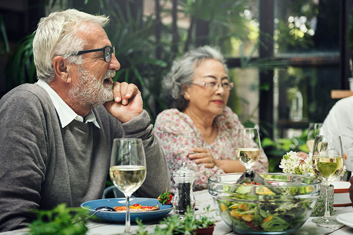 Older couple sitting at a table during a meal, portraying future MIL branding bride-to-be as stupid in a family setting.