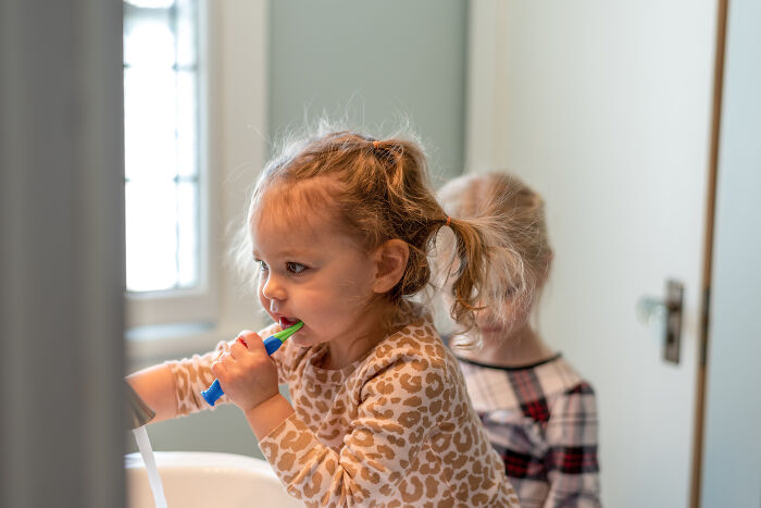Two young children in a bathroom, one brushing teeth, illustrating practical parenting hacks for daily routines.