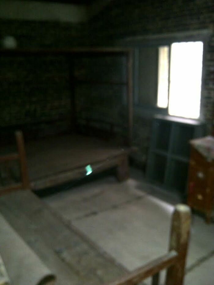 Dimly lit room with old wooden bed frames and rustic furniture, evoking strange and unexplained histories atmosphere.