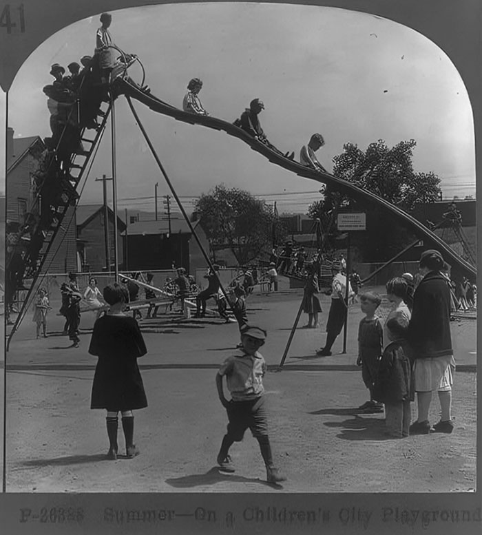 Historic playground photo showing children playing on high slide and swings, highlighting risky childhood play of the past.