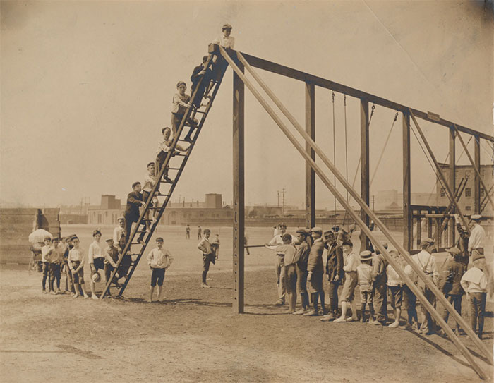 Historic photo of a playground showing children climbing and waiting on unsafe old playground equipment.