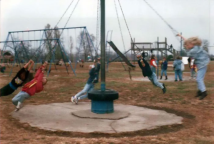 Children swinging on vintage playground equipment in a historic photo showing how risky being a kid back then was.