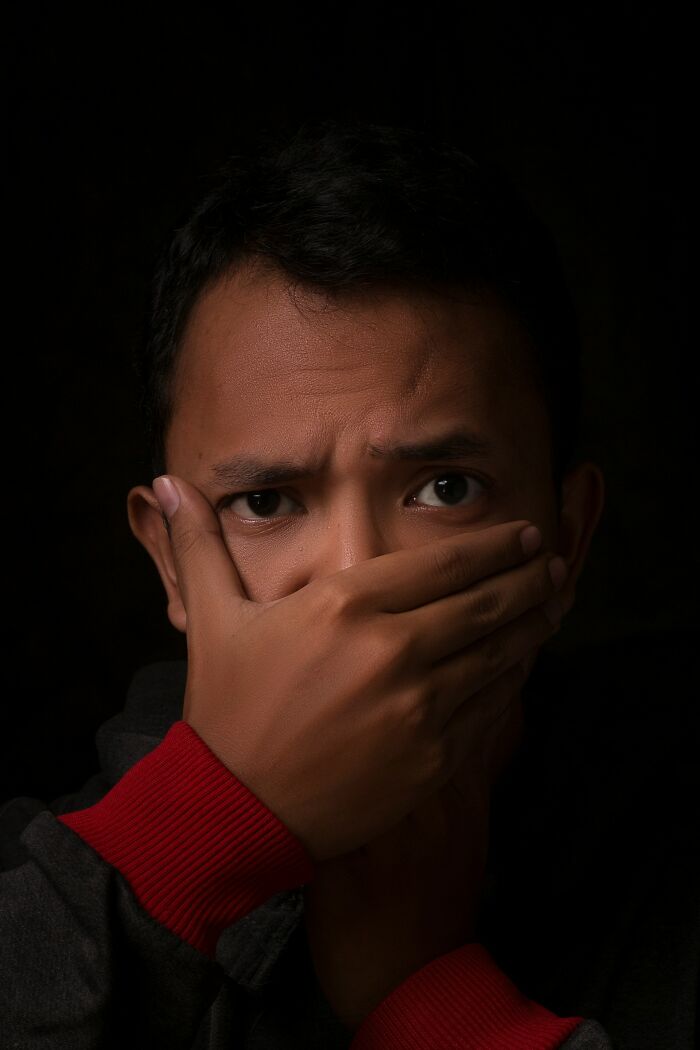 Man alone at home with scared expression covering mouth in dark setting depicting home alone horror moment