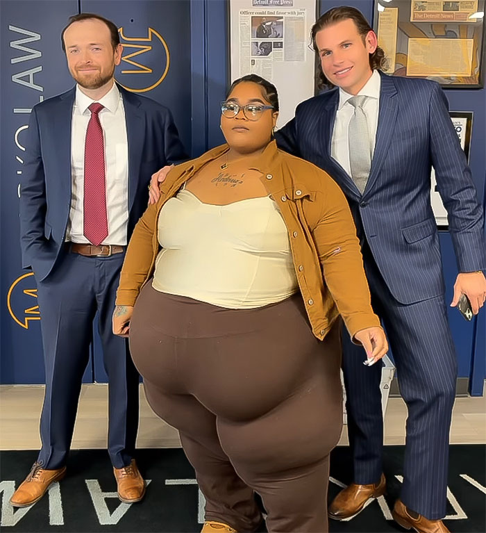 Rapper with two men in suits posing at law office after Lyft driver denied ride due to her weight lawsuit settlement.