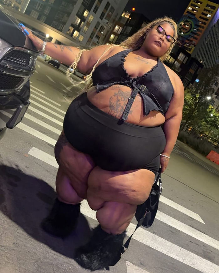 Plus-size woman posing by a car at night, related to rapper lawsuit settlement with Lyft after ride denial over weight.