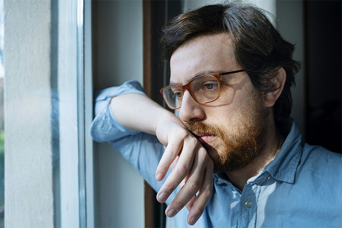 Man with glasses looking pensive by a window, reflecting on defending his daughter&rsquo;s room over fianc&eacute;e&rsquo;s future plans.
