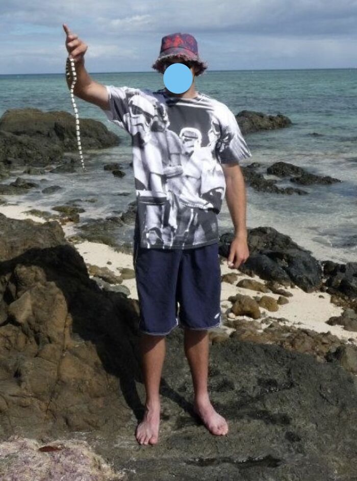 Person standing barefoot on rocky beach holding a snake, illustrating people who came close to death and survived.