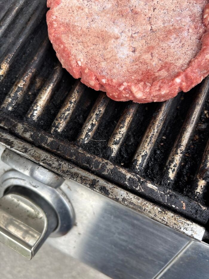 Raw burger patty cooking on a grill, illustrating the concept of anything edible once and close encounters with danger.