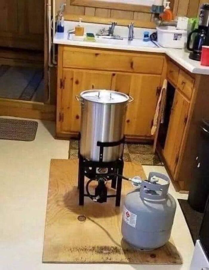 Propane burner with large cooking pot set up indoors on wooden board in a kitchen, illustrating close call death near edible cooking.