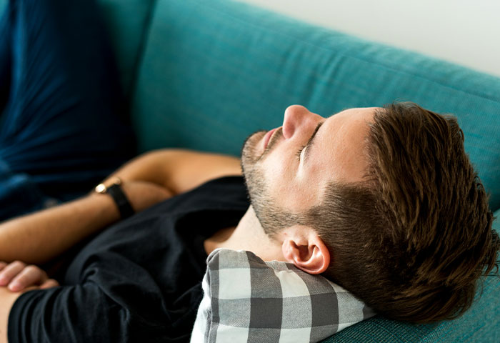 Man with beard resting on a couch pillow, representing poor hygiene and uncomfortable partner reactions.