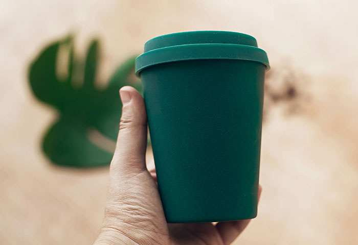 Hand holding a dark green reusable cup with a lid, highlighting concerns related to personal hygiene habits.