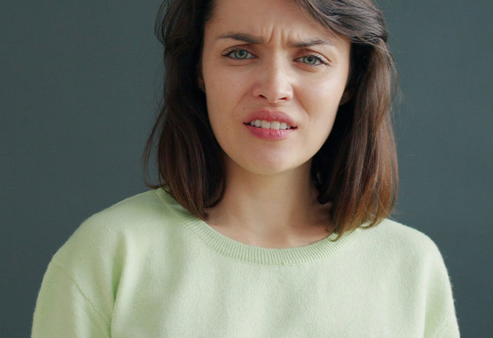 Woman with brown hair wearing a light green sweater showing a disgusted reaction to bad hygiene affecting her partner.