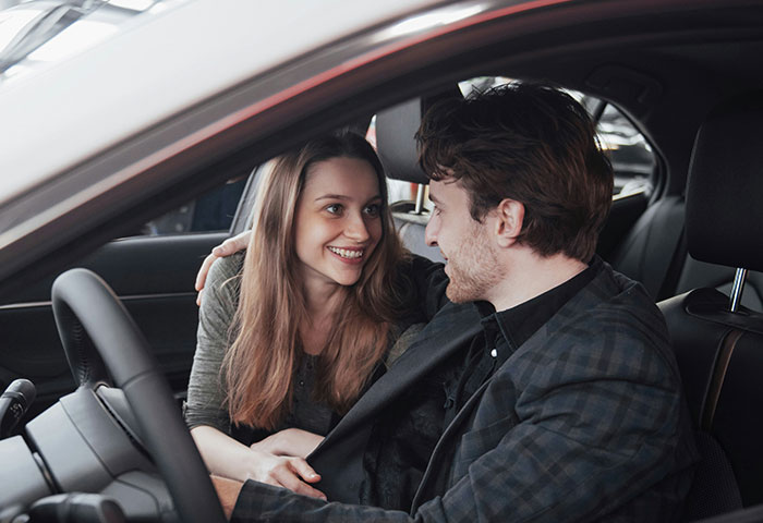 A couple sitting in a car, smiling and looking at each other, illustrating issues with hygiene affecting partners.