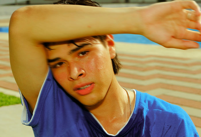 Young man wiping sweat from face outdoors, illustrating poor hygiene causing discomfort and gagging in partners.