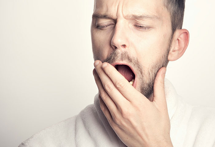 Man covering his mouth while yawning, illustrating poor hygiene and discomfort related to personal care issues.