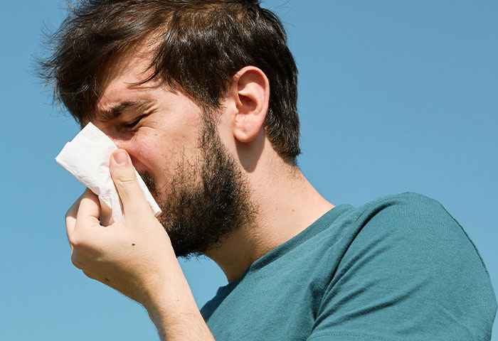 Man with a beard in a teal shirt covering his nose with a tissue, highlighting poor hygiene causing partner discomfort.