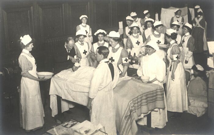 Group of nurses and medical staff performing surgery in an old-school medical setting with vintage equipment and attire.