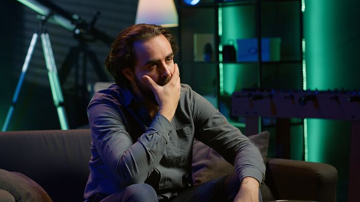 Man looking thoughtful and concerned while sitting on a couch, illustrating the impact of darkest family secrets discovered.