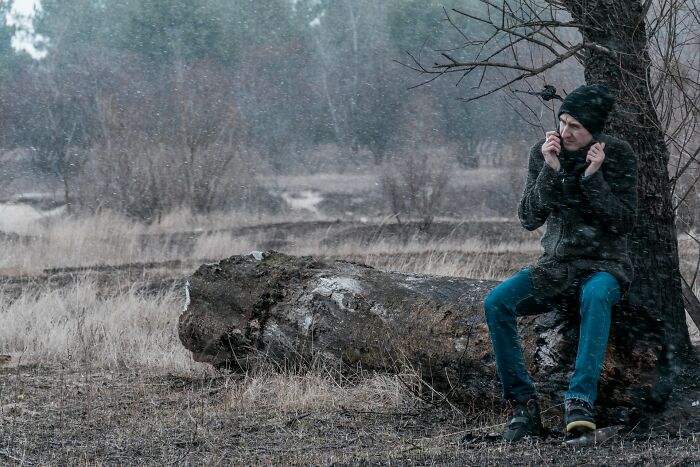 Man sitting alone by a tree in the rain, looking cold and isolated, illustrating sudden ways people get fired.