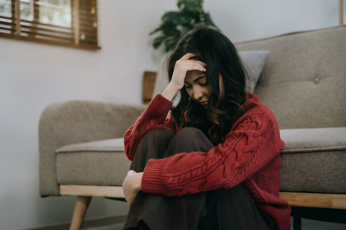 Woman in a red sweater sitting on the floor, looking distressed, representing people who would never admit secrets in real life.
