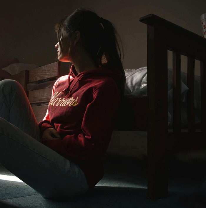 Young woman in red hoodie sitting on floor next to bed, reflecting on wife leaving toddlers behind and husband picking up pieces.