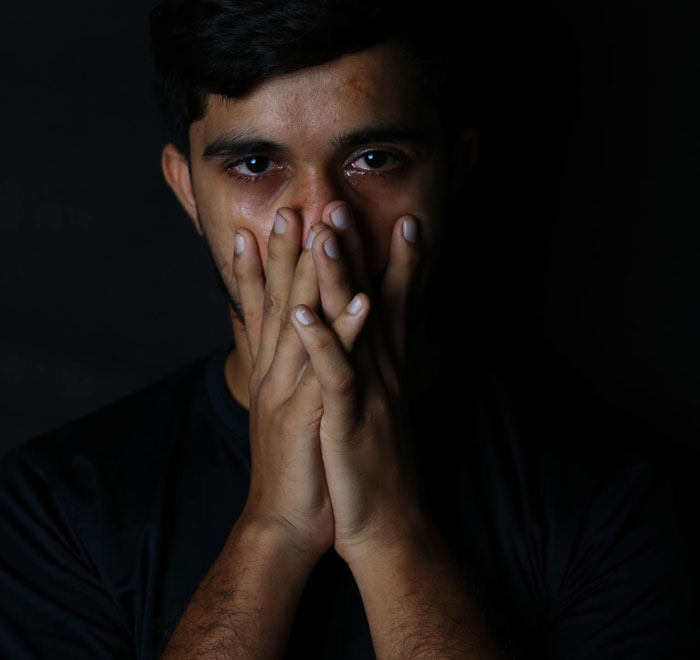 Man with tearful eyes covering his mouth in dark background, symbolizing husband left picking up the pieces after wife leaves toddlers.