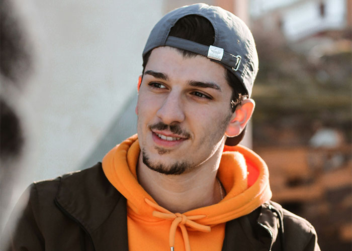 Young landlord wearing a backward cap and orange hoodie, looking confident after getting rid of horrible tenants.