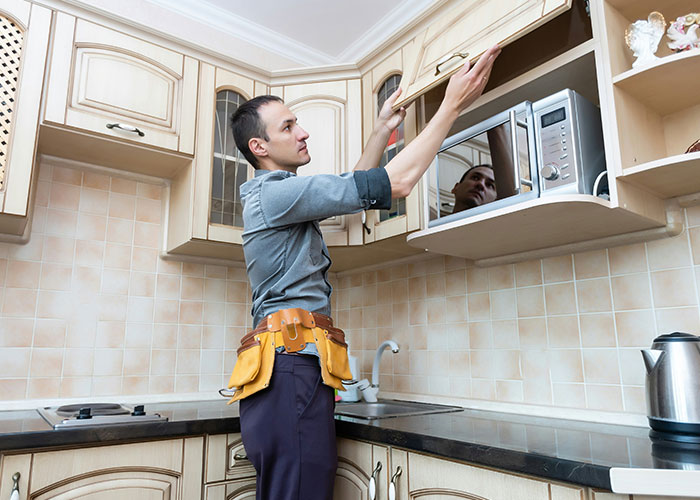 Man in tool belt inspecting kitchen cabinets, symbolizing landlord taking action after getting rid of horrible tenants.