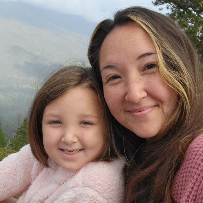 Disney influencer mother and daughter smiling outdoors with a forest and mountain background in soft natural light