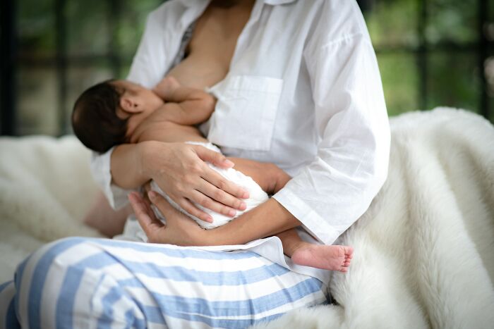Mother breastfeeding baby indoors, highlighting breastfeeding stigma and health risks linked to pumping breast milk at airports.
