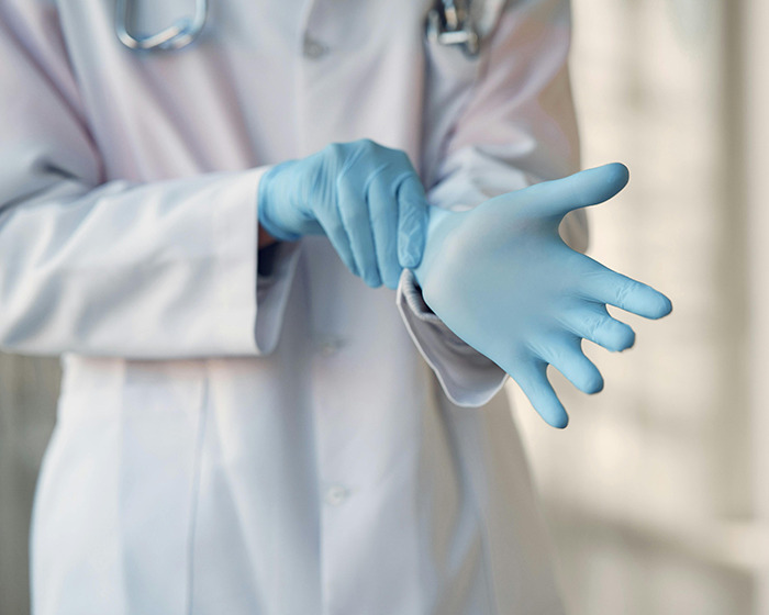 Doctor putting on blue surgical gloves in a hospital setting, related to doctor caught getting intimate with nurse news.