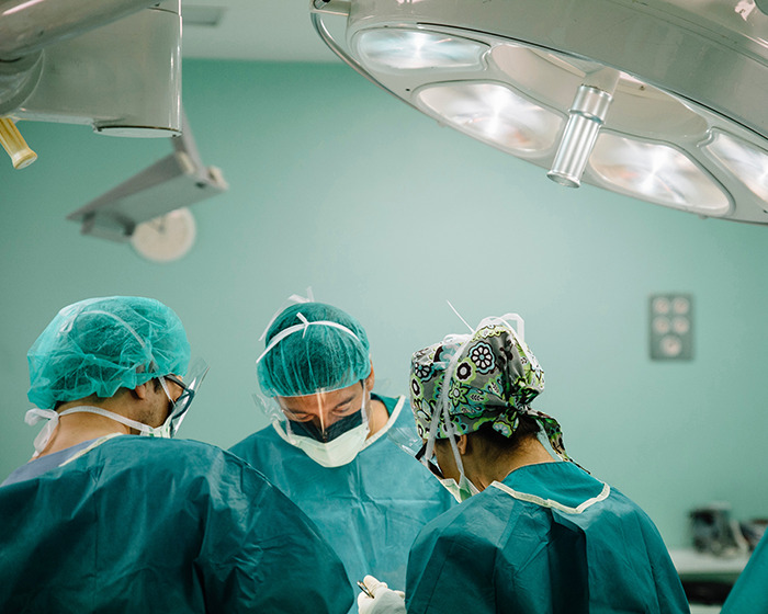 Three medical professionals in surgical attire focused on procedure under bright operating room lights, doctor and nurse present.