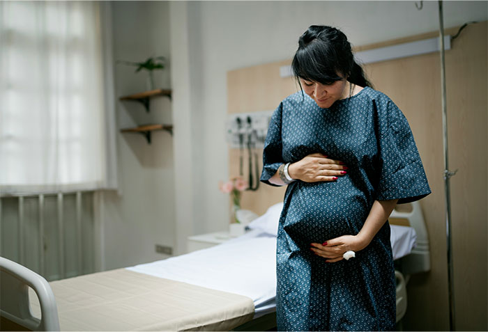Pregnant woman in hospital gown holding belly, illustrating common health myths doctors often expose.